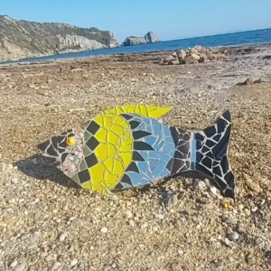 Χειροποίητο μωσαϊκό ψάρι Zizania από ανακυκλωμένα κεραμικά και γυαλί σε παραλία.