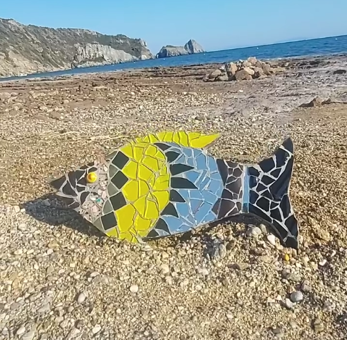 Χειροποίητο μωσαϊκό ψάρι Zizania από ανακυκλωμένα κεραμικά και γυαλί σε παραλία.